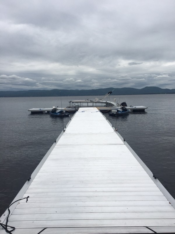 Aluminum floating dock extending into calm lake with boats and mountains in background