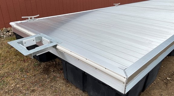 Close-up of aluminum floating dock deck with float drums and hinge hardware on ground